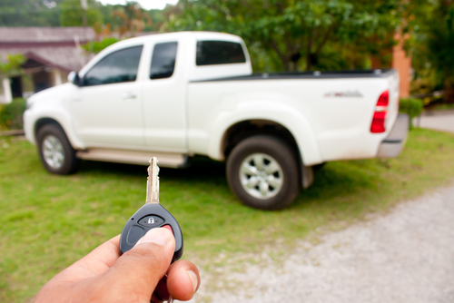 A man's hand holding a key pointing to a white dodge ram truck